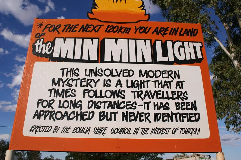 An orange roadside sign in outback Queensland announcing the land of the Min Min light, an unsolved mystery that follows travellers