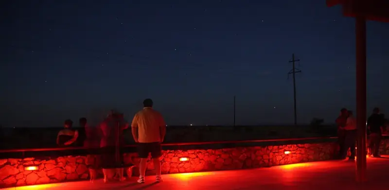 Visitors on the Viewing Area platform at night, lit by low red lights, looking out over the dark flat