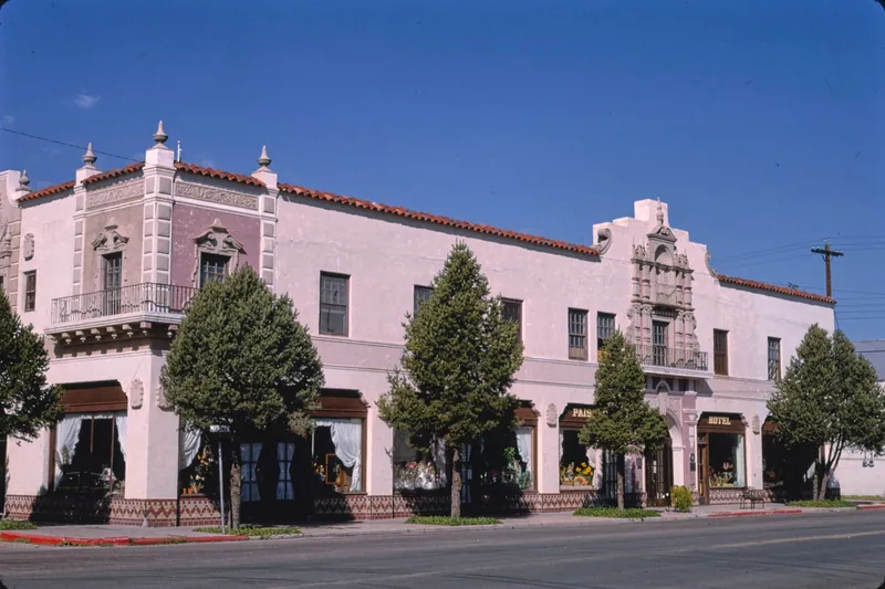 A two-storey pink stucco hotel with ornate Spanish-style trim and trees along the sidewalk