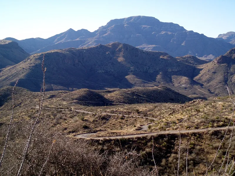 A dirt road switchbacking down into a canyon below rugged, bare volcanic mountains
