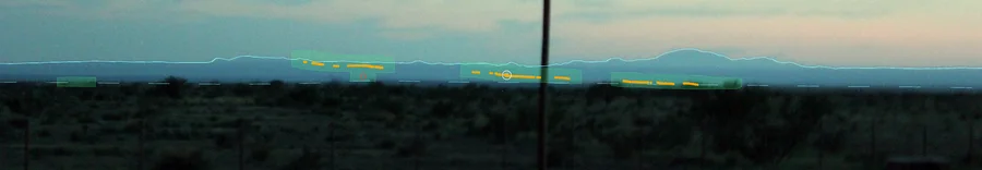 Dusk photo of the flat with the Chinati Mountains on the horizon, a thin cyan line traced along the mountain tops, green boxes and orange dots along the base of the mountains, and a white ring around a small light that sits on the orange dots