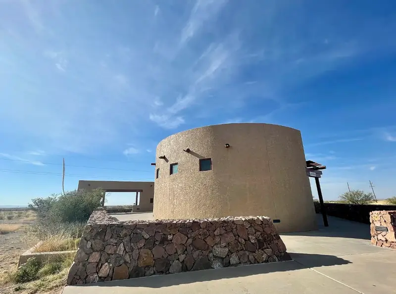 The round adobe-style Marfa Lights Viewing Area building and stone wall under a blue sky